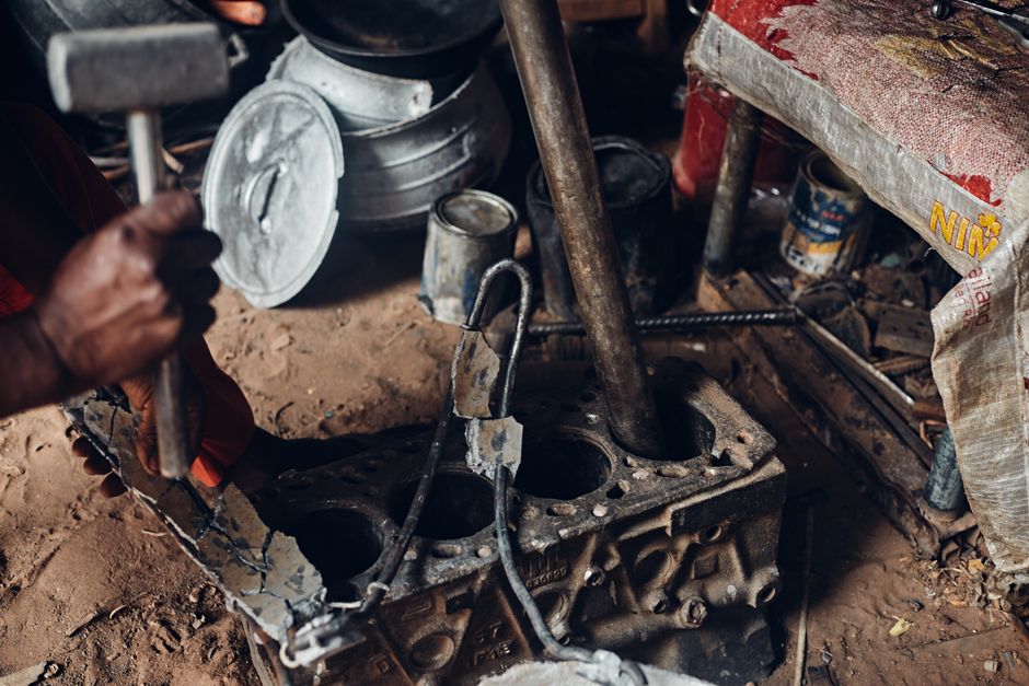 Mechanic working with a hammer on an engine block in a rustic workshop setting.